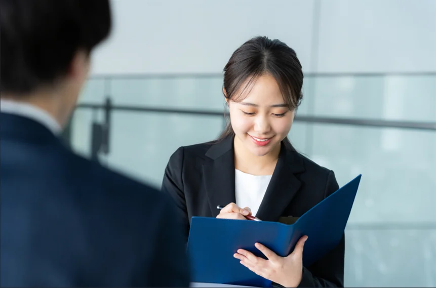 青いファイルを手に、笑顔で相談内容を書き留める女性カウンセラー